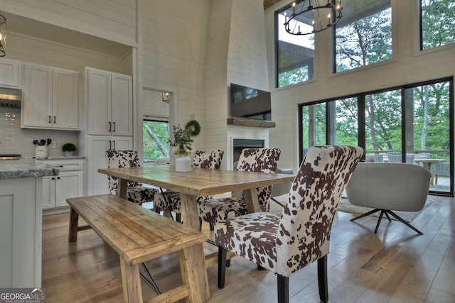 dining room with hardwood / wood-style floors, a fireplace, a towering ceiling, and a chandelier