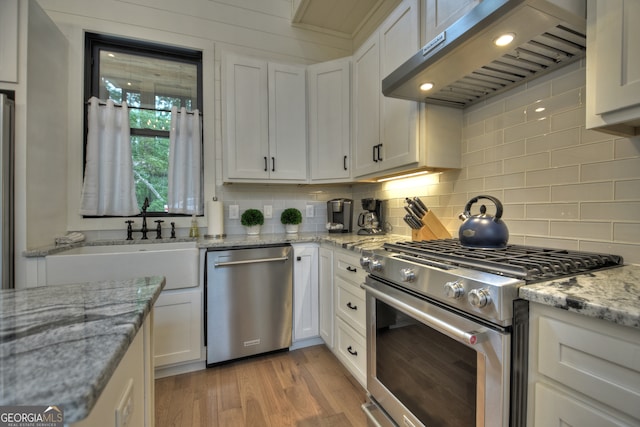 kitchen featuring white cabinets, light stone countertops, stainless steel appliances, exhaust hood, and light hardwood / wood-style flooring