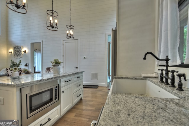 kitchen with hanging light fixtures, stainless steel microwave, sink, and light stone counters