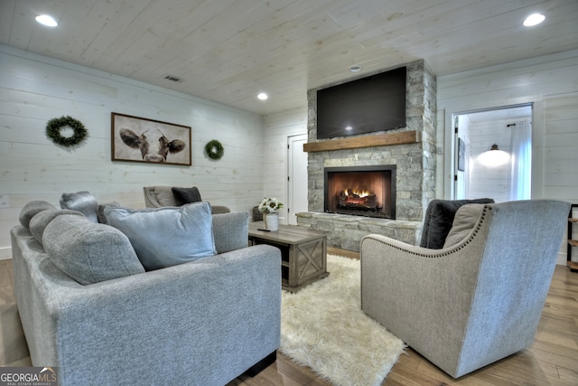 living room featuring light wood-type flooring, wood ceiling, a fireplace, and wooden walls