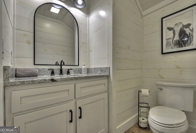 bathroom featuring wooden walls, vanity, and toilet