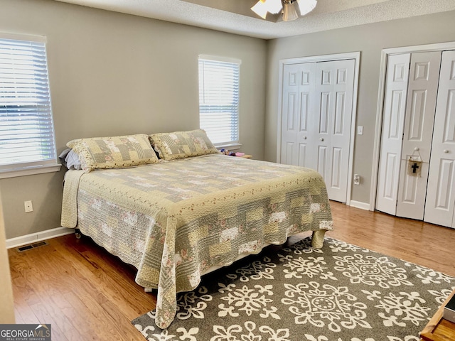 bedroom with ceiling fan, two closets, baseboards, wood finished floors, and visible vents