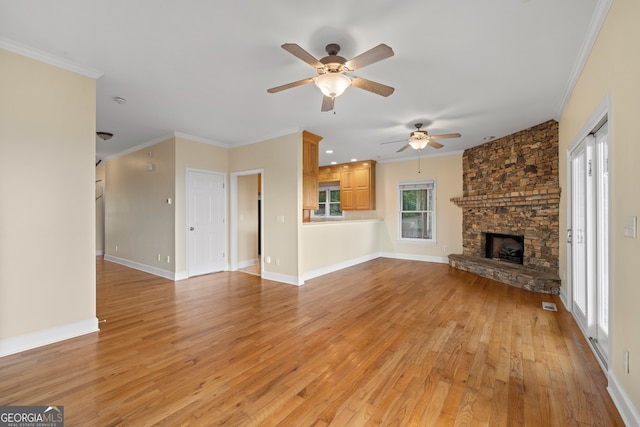 unfurnished living room featuring light hardwood / wood-style floors, ornamental molding, a stone fireplace, and ceiling fan