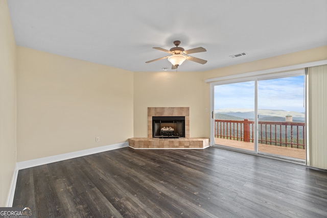 unfurnished living room with dark wood-type flooring, a mountain view, a tiled fireplace, and ceiling fan