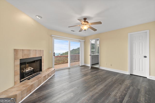 unfurnished living room with a tiled fireplace, dark wood-type flooring, and ceiling fan