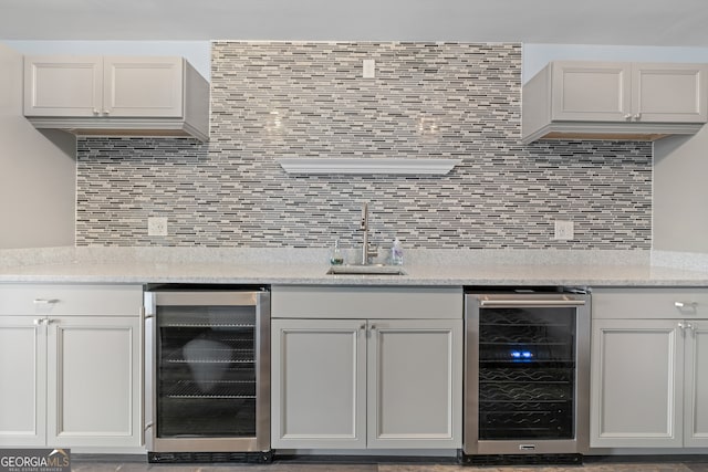 bar featuring wine cooler, sink, decorative backsplash, and light stone counters