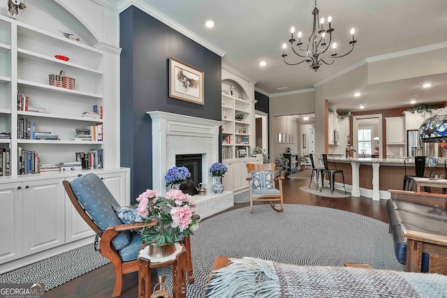 living room featuring built in shelves, wood-type flooring, a brick fireplace, a chandelier, and crown molding