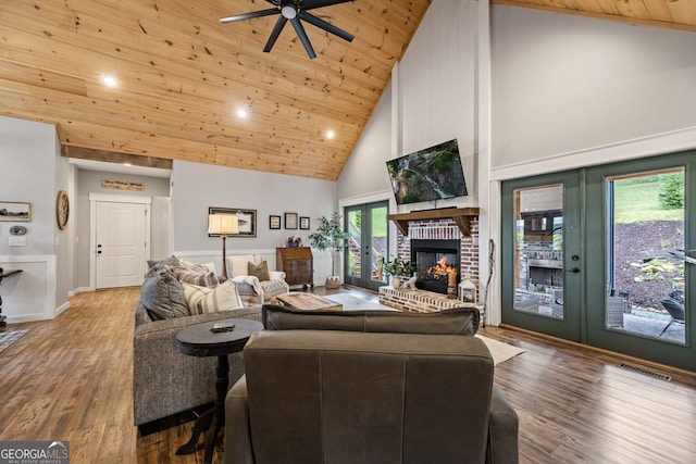 living room featuring wood-type flooring, high vaulted ceiling, a brick fireplace, ceiling fan, and french doors