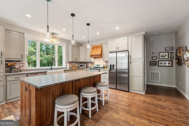 kitchen with pendant lighting, a kitchen island, custom exhaust hood, light hardwood / wood-style flooring, and appliances with stainless steel finishes