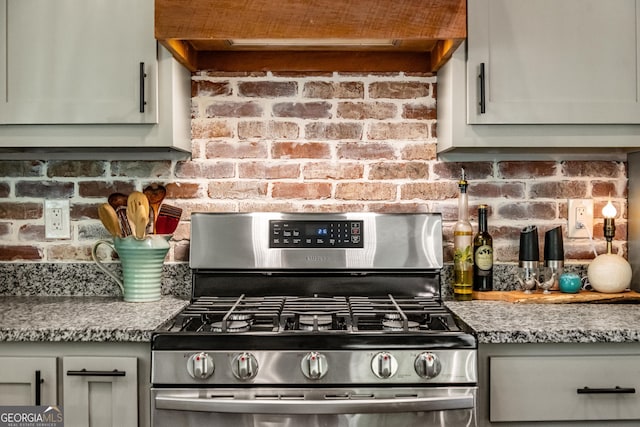 kitchen with light stone counters, brick wall, gas range, gray cabinets, and range hood