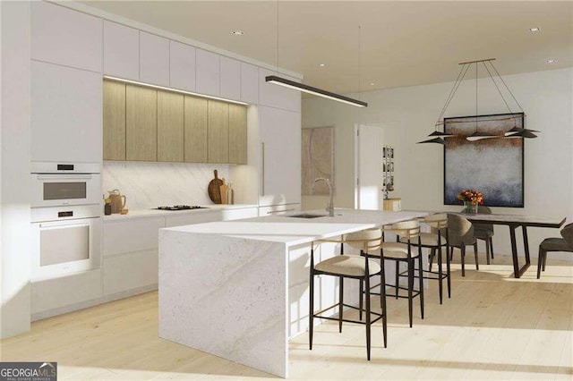 kitchen featuring white cabinets, light hardwood / wood-style flooring, a center island with sink, double oven, and sink