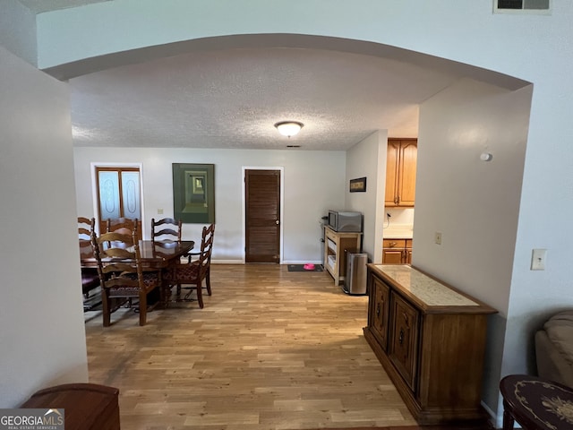 dining space featuring baseboards, light wood-type flooring, a textured ceiling, visible vents, and arched walkways