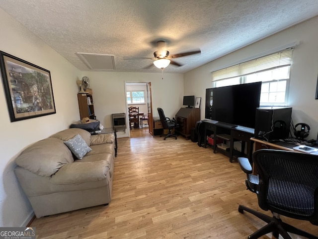 living area featuring light wood-type flooring, a ceiling fan, a textured ceiling, and heating unit