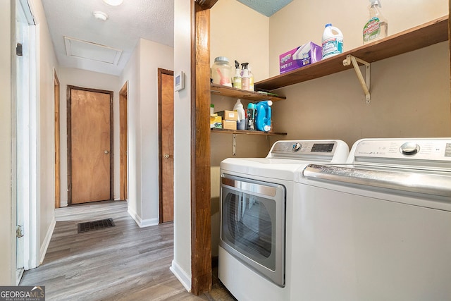 laundry area with light wood-type flooring, washer and dryer, and a textured ceiling