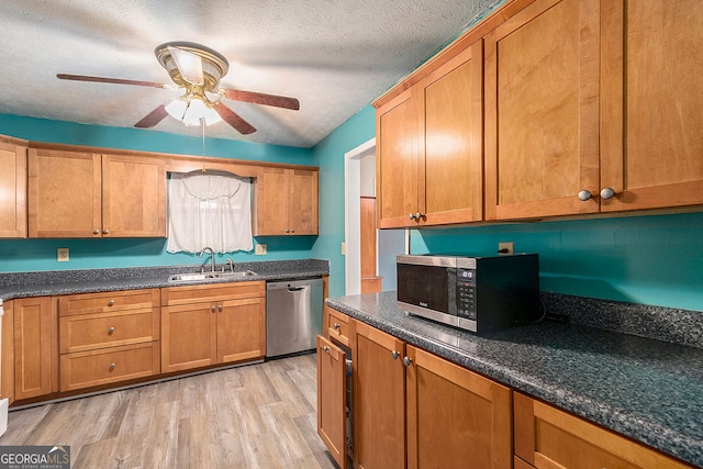 kitchen with ceiling fan, sink, a textured ceiling, stainless steel appliances, and light wood-type flooring