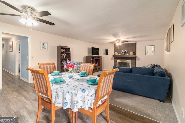 dining area with hardwood / wood-style flooring, a fireplace, ceiling fan, and a textured ceiling