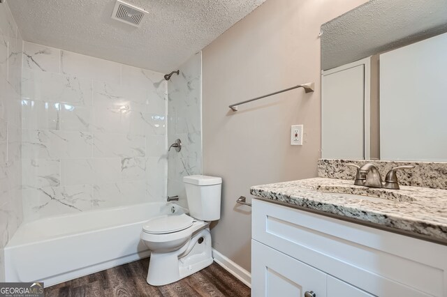 full bathroom featuring tiled shower / bath, vanity, wood-type flooring, a textured ceiling, and toilet