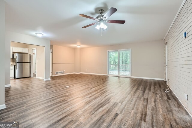 unfurnished living room with wood-type flooring, ceiling fan, and brick wall