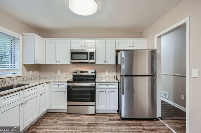 kitchen featuring white cabinetry, appliances with stainless steel finishes, light stone counters, and dark wood-type flooring