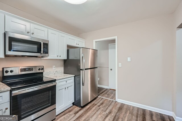 kitchen with light stone countertops, stainless steel appliances, white cabinets, and light hardwood / wood-style flooring