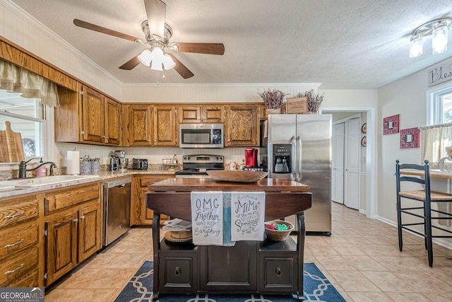 kitchen with ceiling fan, sink, ornamental molding, a textured ceiling, and stainless steel appliances