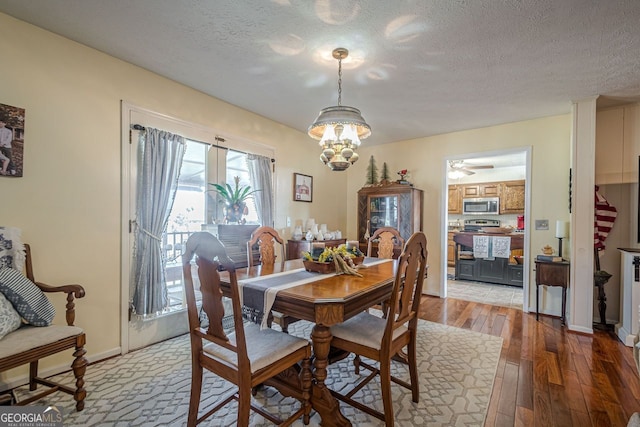 dining space with ceiling fan with notable chandelier, light wood-type flooring, and a textured ceiling