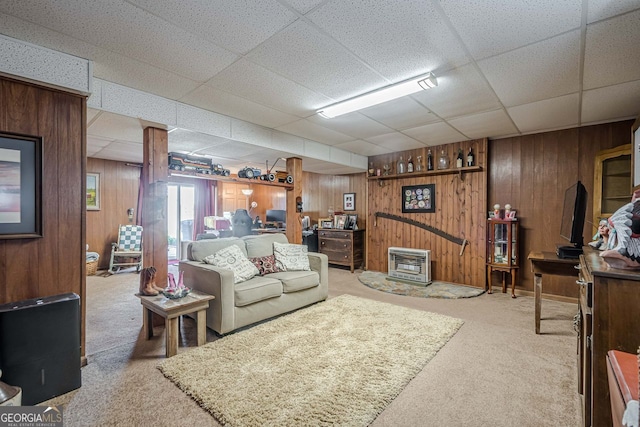 carpeted living room with a drop ceiling, wood walls, and heating unit