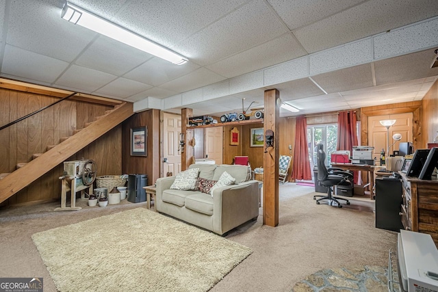 carpeted living room with a paneled ceiling and wood walls