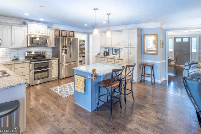 kitchen with appliances with stainless steel finishes, hanging light fixtures, white cabinetry, crown molding, and a center island