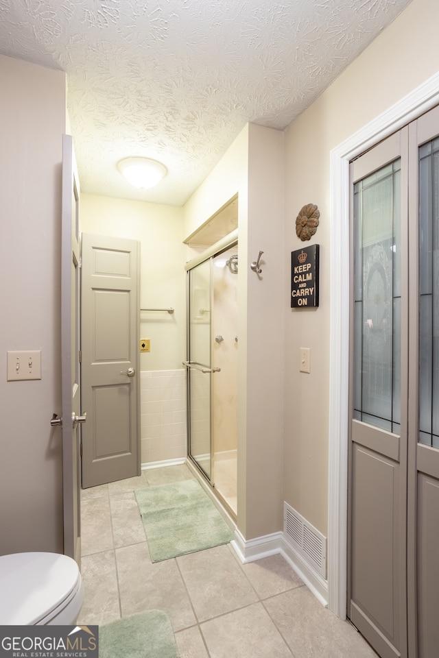 bathroom with a textured ceiling, toilet, tile patterned floors, and a shower with shower door