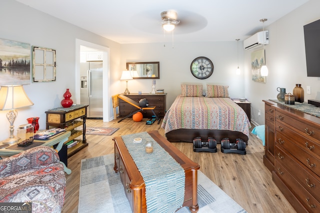 bedroom with light hardwood / wood-style floors, connected bathroom, an AC wall unit, ceiling fan, and stainless steel fridge with ice dispenser