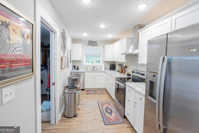 kitchen with light stone counters, light hardwood / wood-style floors, white cabinets, wall chimney exhaust hood, and stainless steel appliances