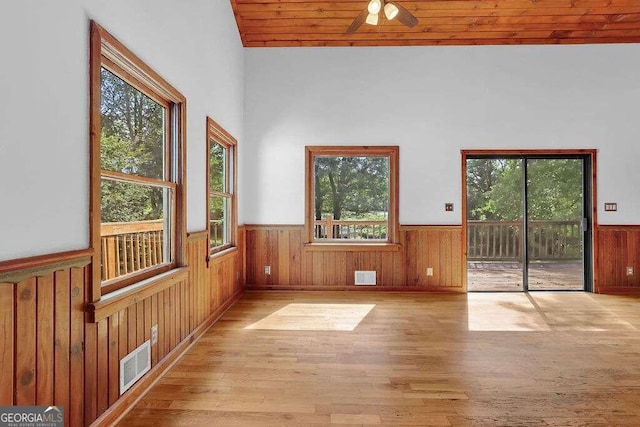 spare room featuring light hardwood / wood-style floors, wooden walls, a towering ceiling, ceiling fan, and wooden ceiling