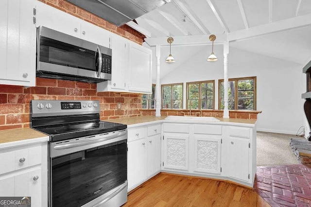 kitchen featuring pendant lighting, sink, lofted ceiling, white cabinetry, and appliances with stainless steel finishes