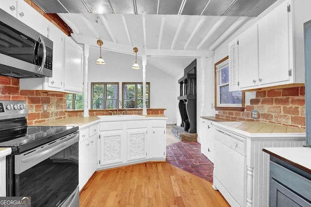 kitchen with sink, white cabinets, lofted ceiling, appliances with stainless steel finishes, and decorative light fixtures