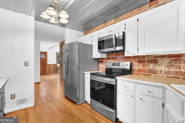 kitchen with stainless steel appliances, white cabinetry, a chandelier, and light wood-type flooring