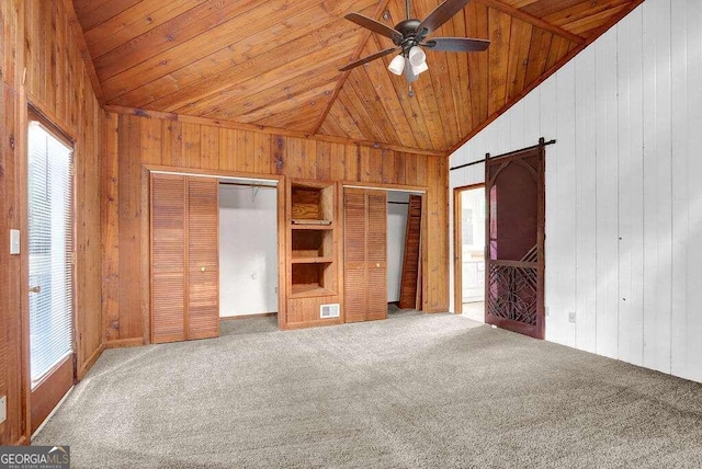 unfurnished bedroom featuring multiple closets, wood walls, carpet flooring, and a barn door