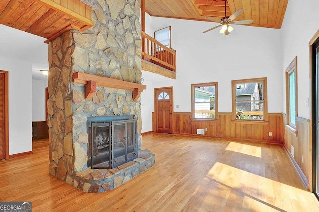 unfurnished living room featuring ceiling fan, light hardwood / wood-style floors, a stone fireplace, wooden ceiling, and vaulted ceiling