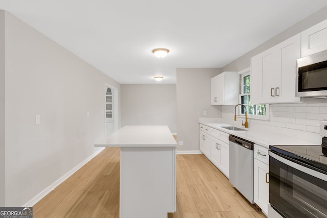 kitchen with light wood-type flooring, sink, white cabinetry, a kitchen island, and appliances with stainless steel finishes