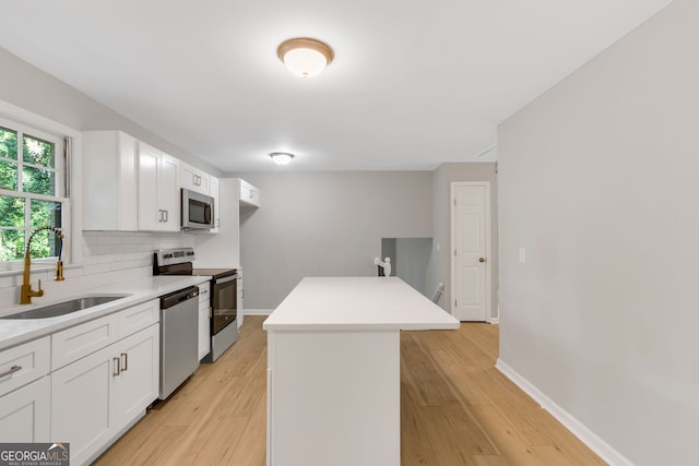 kitchen with light hardwood / wood-style floors, sink, white cabinetry, a kitchen island, and stainless steel appliances