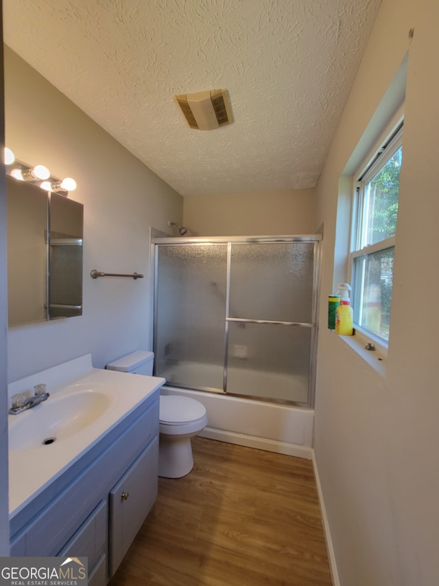 full bathroom featuring vanity, a textured ceiling, bath / shower combo with glass door, hardwood / wood-style flooring, and toilet