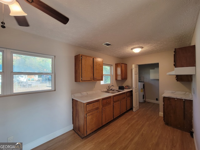 kitchen with light wood-type flooring, a textured ceiling, sink, and electric water heater