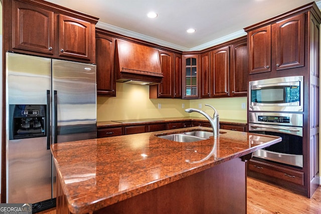 kitchen with sink, custom range hood, light hardwood / wood-style flooring, appliances with stainless steel finishes, and dark stone countertops