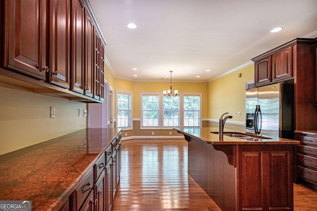 kitchen with stainless steel fridge, an island with sink, light hardwood / wood-style flooring, sink, and a notable chandelier