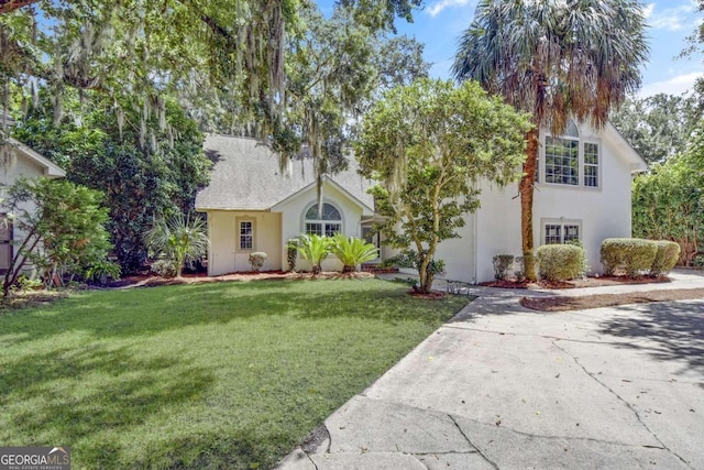 view of front of property with a front yard, roof with shingles, and stucco siding