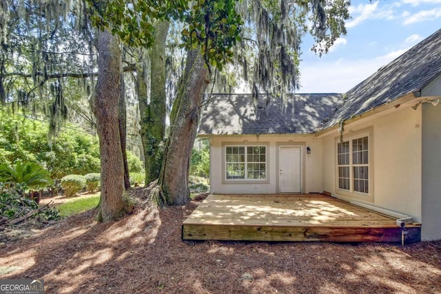 entrance to property featuring a deck, roof with shingles, and stucco siding