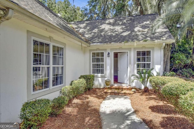 doorway to property with stucco siding and roof with shingles