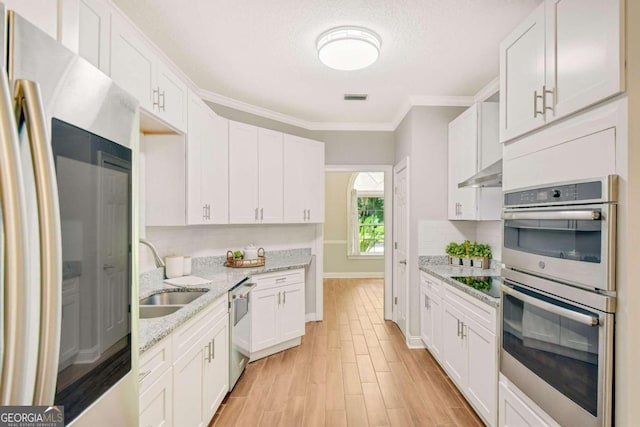 kitchen featuring light stone counters, under cabinet range hood, stainless steel appliances, a sink, and white cabinetry