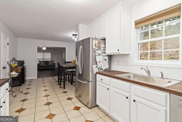 kitchen featuring white cabinets, sink, stainless steel refrigerator, and wooden counters