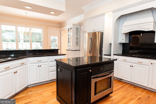 kitchen with white cabinets, a kitchen island, stainless steel appliances, light wood-type flooring, and ornamental molding